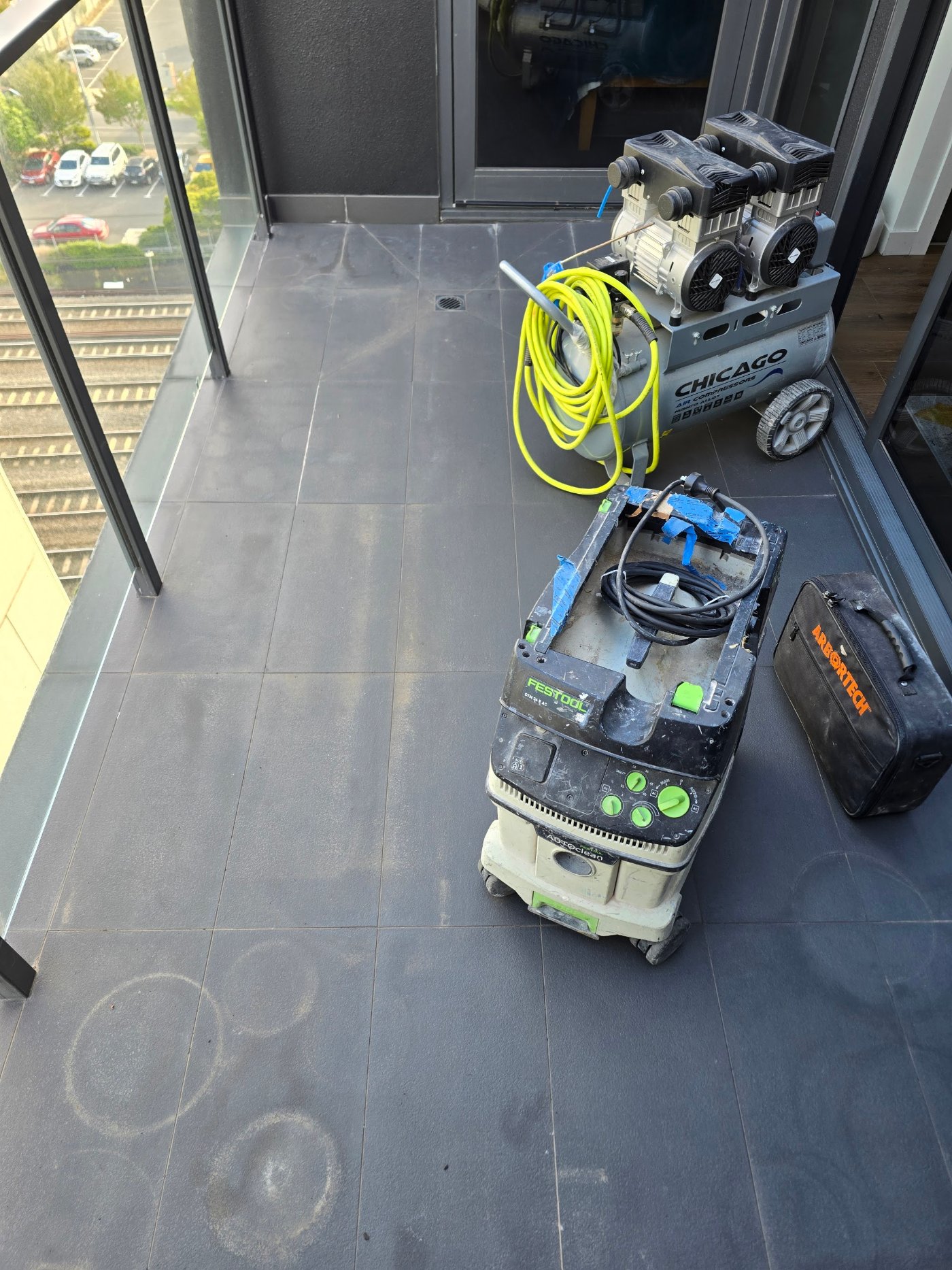 Compressor and dust extraction set up on an apartment balcony before grout removal
